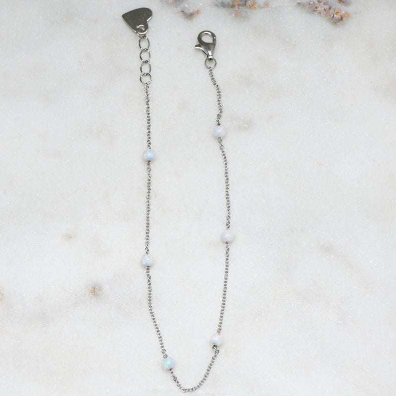 May include: A silver chain bracelet with five white opal beads. The bracelet has a heart-shaped clasp.