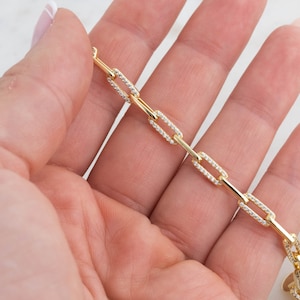 May include: A gold chain bracelet with small square links, each link is encrusted with tiny clear cubic zirconia stones.