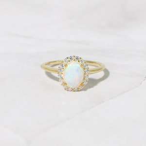 Pode incluir: Um anel de ouro com uma gema de opala branca cercada por um halo de diamantes menores.