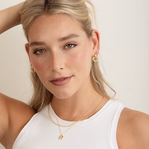 model wearing gold knot hoop earrings with small studs, paired with a gold rice bead necklace and starburst medallion