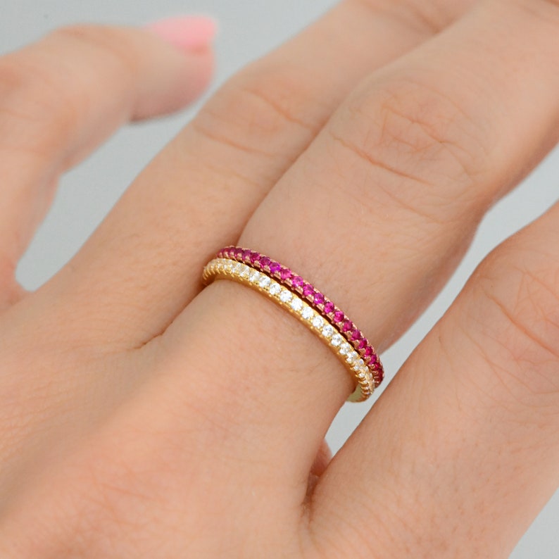 May include: Two gold rings with a row of small pink gemstones and a row of small white gemstones.