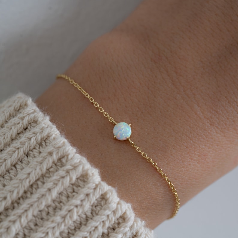 May include: A delicate gold chain bracelet with a single white opal gemstone.