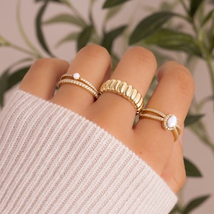 model wearing gold stacking rings and opal stacking rings featuring an opal solitaire stone dainty ring, a cubic zirconia eternity ring, a gold statement ring, and and oval opal ring