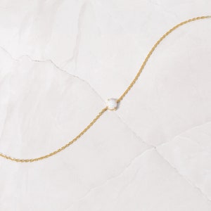 May include: A delicate gold chain necklace with a single white opal gemstone pendant.