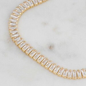 Pu&ograve; includere: Una collana a catena d'oro con cristalli trasparenti a forma di baguette.