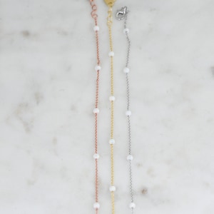 May include: Three delicate gold chains with small white beads. The chains are in rose gold, yellow gold, and silver.