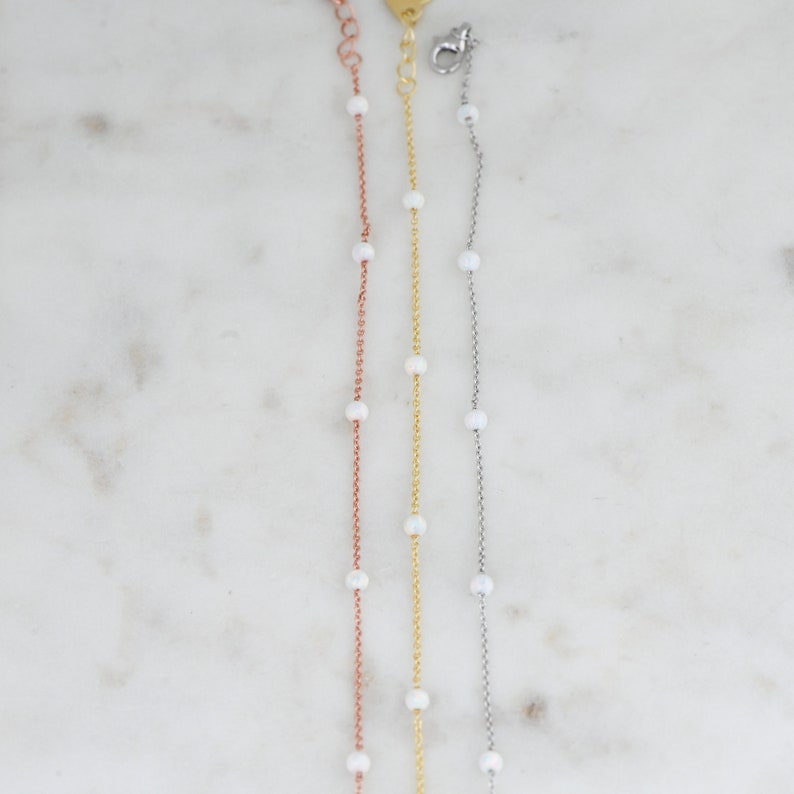 May include: Three delicate gold chains with small white beads. The chains are in rose gold, yellow gold, and silver.