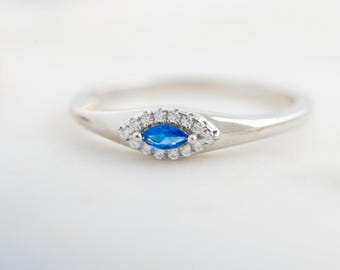 May include: A silver ring with a blue marquise-shaped gemstone surrounded by a halo of smaller clear gemstones.