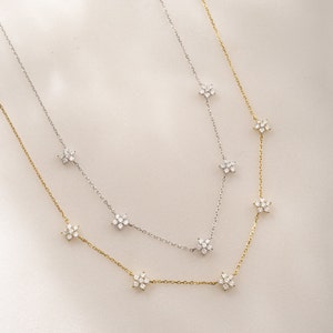 Pu&ograve; includere: Due delicate collane con una catena d'argento e oro con piccoli ciondoli a forma di fiore con pietre scintillanti trasparenti.