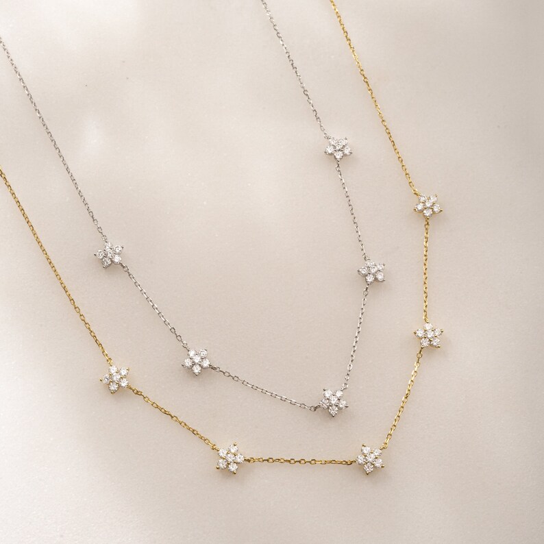 Pu&ograve; includere: Due delicate collane con una catena d'argento e oro con piccoli ciondoli a forma di fiore con pietre scintillanti trasparenti.