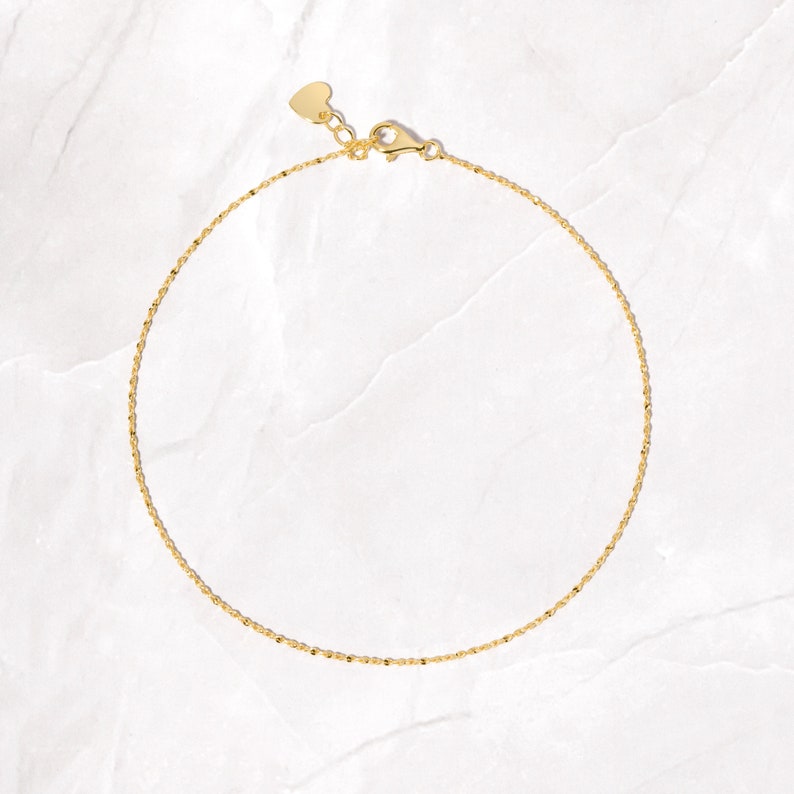 May include: A delicate gold chain anklet with a heart-shaped clasp.