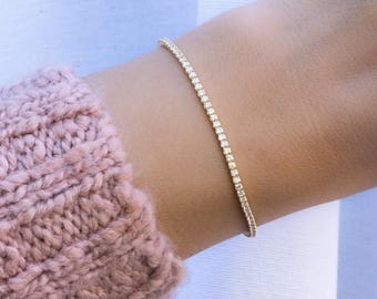 Puede incluir: Un delicado brazalete de tenis de oro con una fila de pequeñas piedras de circonita cúbica transparentes.