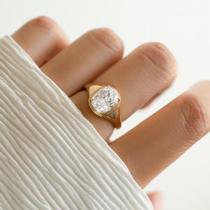 Model image of an elongated diamond cushion cut ring in gold plating worn on models hand