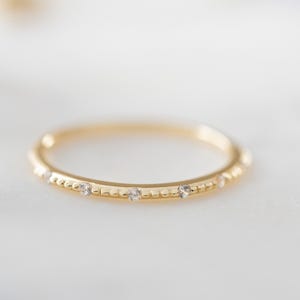 May include: A delicate gold band ring with a beaded edge and small clear stones set along the top.