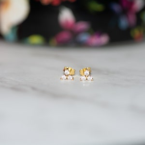 May include: A pair of gold stud earrings with three small, clear cubic zirconia stones arranged in a triangular shape.