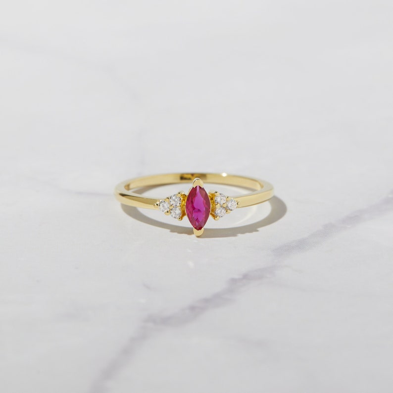 Op de afbeelding: Een gouden ring met een marquise-vormige robijn en kleine ronde diamanten op de band.