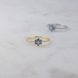 May include: A gold ring with a blue and white flower design. The ring is set with small, sparkling stones.