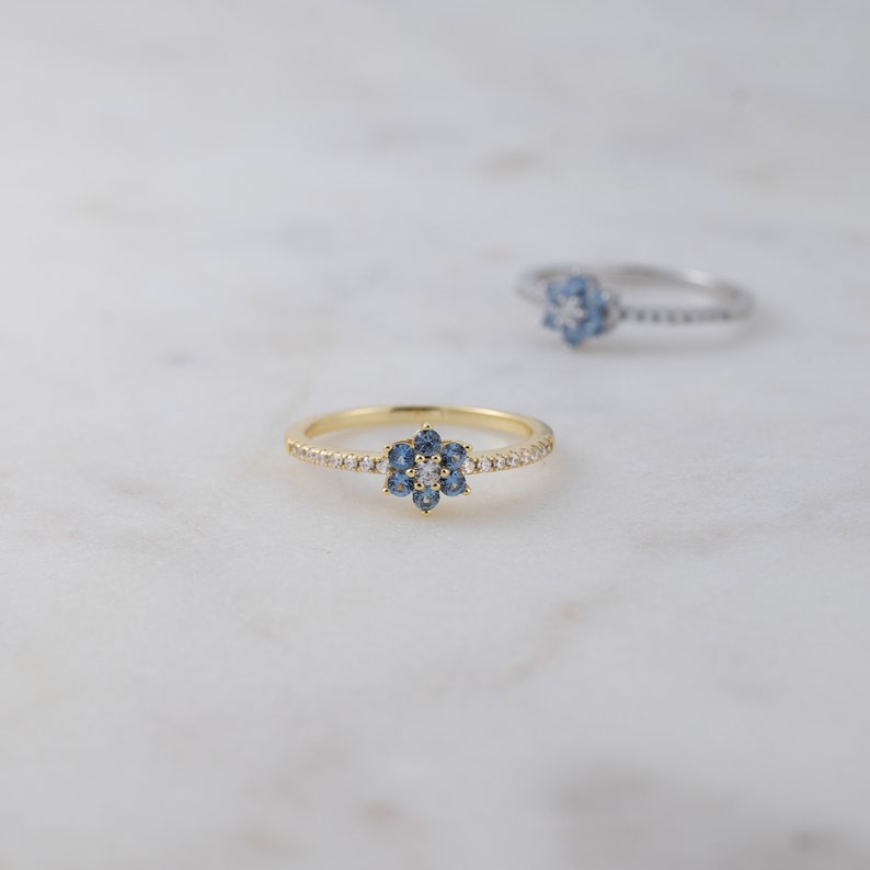May include: A gold ring with a blue and white flower design. The ring is set with small, sparkling stones.