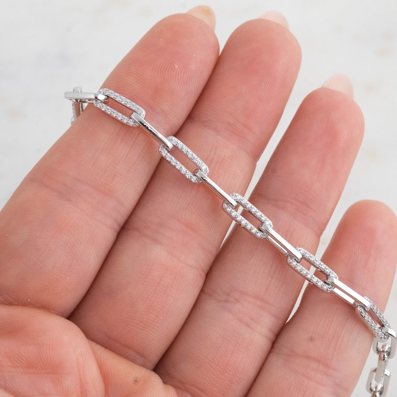 May include: A silver chain bracelet with small, clear cubic zirconia stones set into each link. The chain is made of a series of connected rectangular links.