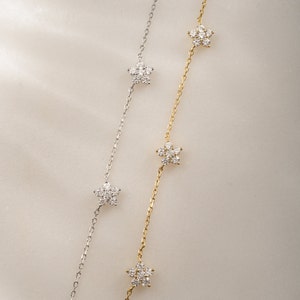 Pu&ograve; includere: Due delicate collane con un design a catena e piccoli ciondoli a forma di fiore incastonati con diamanti scintillanti. Una collana &egrave; d'argento e l'altra &egrave; d'oro.