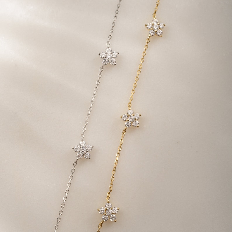 Pu&ograve; includere: Due delicate collane con un design a catena e piccoli ciondoli a forma di fiore incastonati con diamanti scintillanti. Una collana &egrave; d'argento e l'altra &egrave; d'oro.