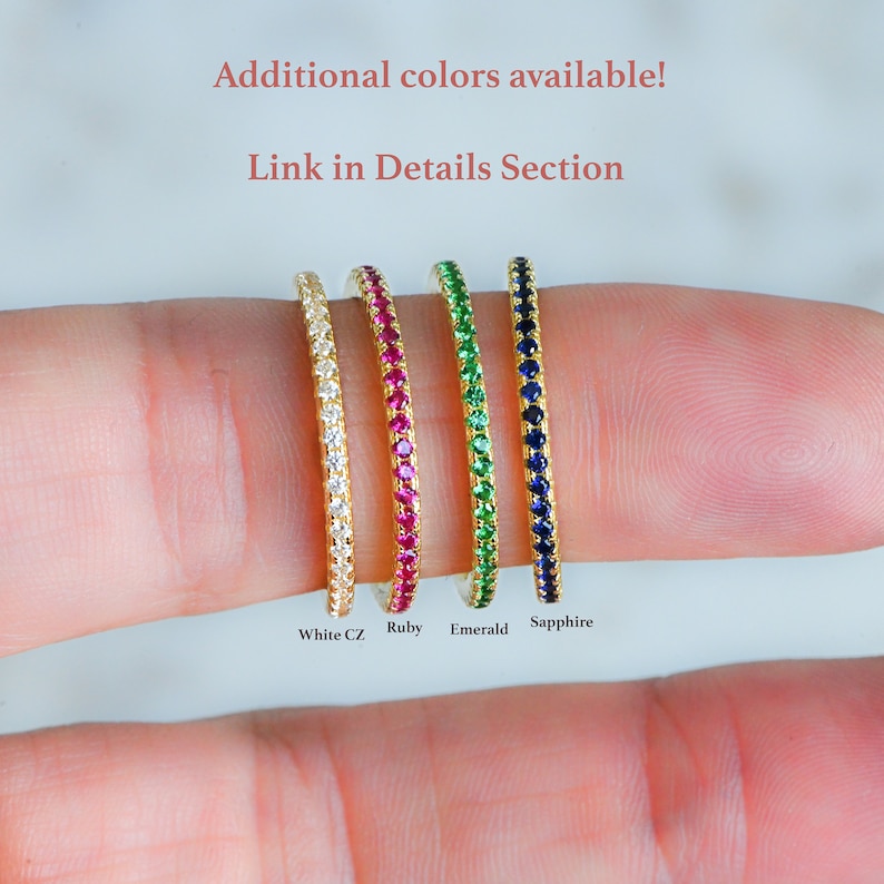 May include: Four gold rings with a single row of gemstones. The rings are lined up from left to right: white CZ, ruby, emerald, and sapphire.