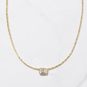 May include: A delicate gold chain necklace with a single, clear, rectangular-shaped gemstone pendant.