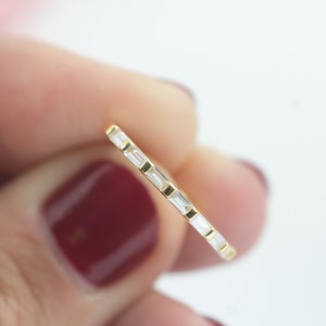 Könnte beinhalten: Ein Goldring mit einer Reihe kleiner, klarer, rechteckiger Steine.