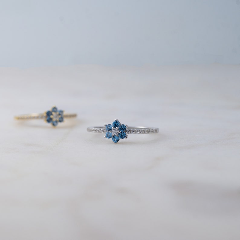 May include: A silver ring with a blue and white flower design. The ring is set with small, sparkling stones.
