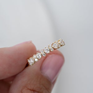Op de afbeelding: Een delicate gouden ring met een cluster van kleine, glinsterende diamanten die in een verspringend patroon zijn gezet.