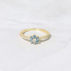 May include: A gold ring with a blue and white flower design. The ring is set with small, sparkling stones.