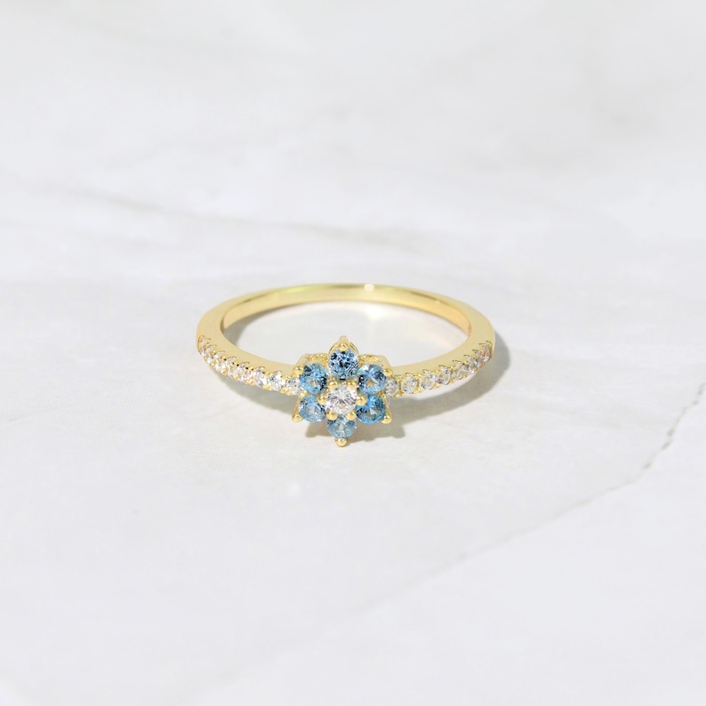 May include: A gold ring with a blue and white flower design. The ring is set with small, sparkling stones.