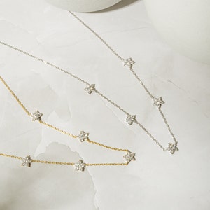 Pu&ograve; includere: Due delicate collane con un design a catena e piccoli ciondoli a forma di fiore con pietre trasparenti. La collana in alto &egrave; d'argento e la collana in basso &egrave; d'oro.