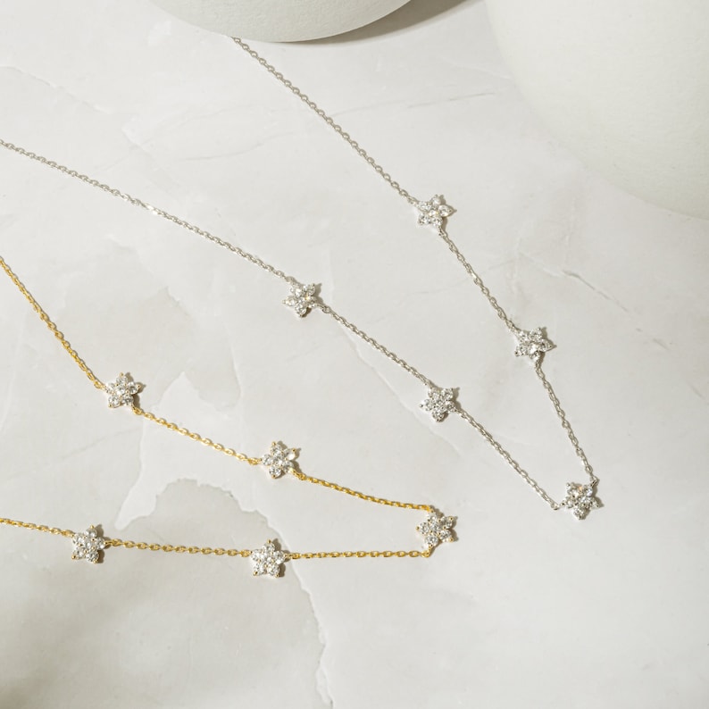 Pu&ograve; includere: Due delicate collane con un design a catena e piccoli ciondoli a forma di fiore con pietre trasparenti. La collana in alto &egrave; d'argento e la collana in basso &egrave; d'oro.