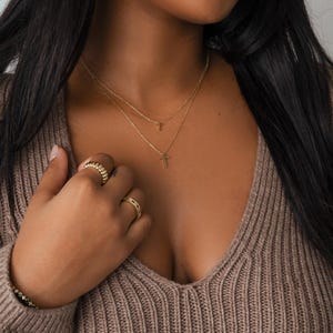 Model wearing layered dainty gold necklaces with tiny cross pendants