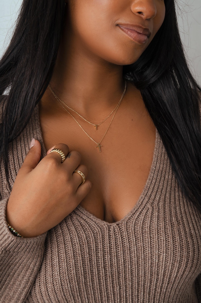 Model wearing layered dainty gold necklaces with tiny cross pendants