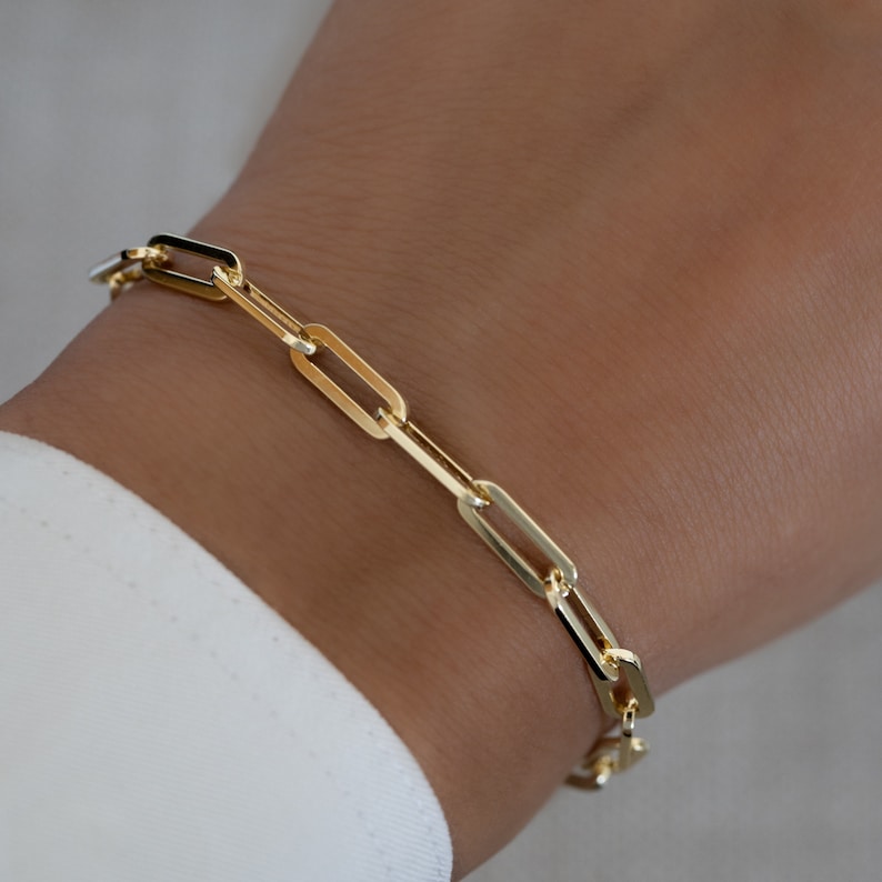 May include: A gold chain bracelet with a link style design. The bracelet is made of a thick, chunky chain with oval-shaped links.