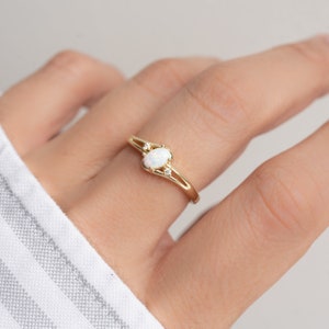May include: A gold ring featuring an oval opal gemstone and two smaller accent stones. The ring has a delicate, open design with a polished finish. The opal has a milky white appearance. The ring is a piece of jewelry.