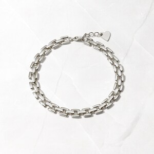 Pode incluir: Um bracelete de corrente de prata com um fecho em forma de cora&ccedil;&atilde;o. A corrente &eacute; feita de elos retangulares entrela&ccedil;ados.
