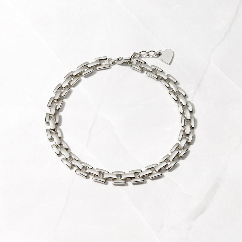Pode incluir: Um bracelete de corrente de prata com um fecho em forma de cora&ccedil;&atilde;o. A corrente &eacute; feita de elos retangulares entrela&ccedil;ados.