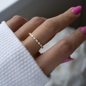 May include: A delicate gold band ring with a row of small, clear pear-shaped stones.