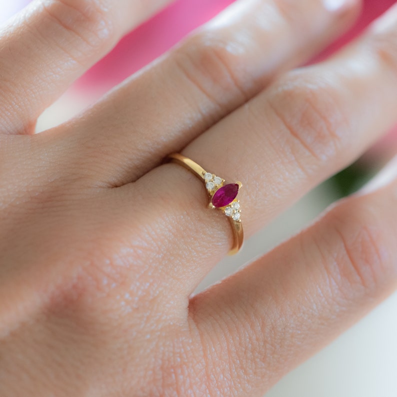 Op de afbeelding: Een gouden ring met een marquise-vormige robijn en kleine ronde diamanten op de band.