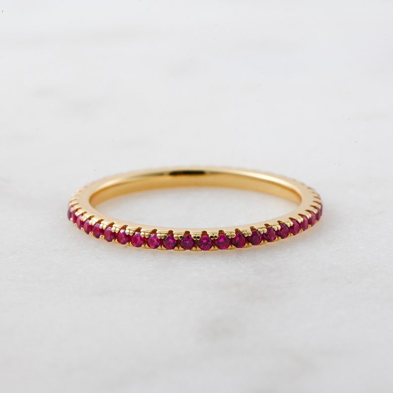 May include: A delicate gold band ring with a row of small red ruby stones.