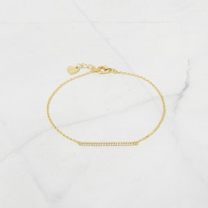 May include: A gold chain bracelet with a thin bar charm set with small clear stones.