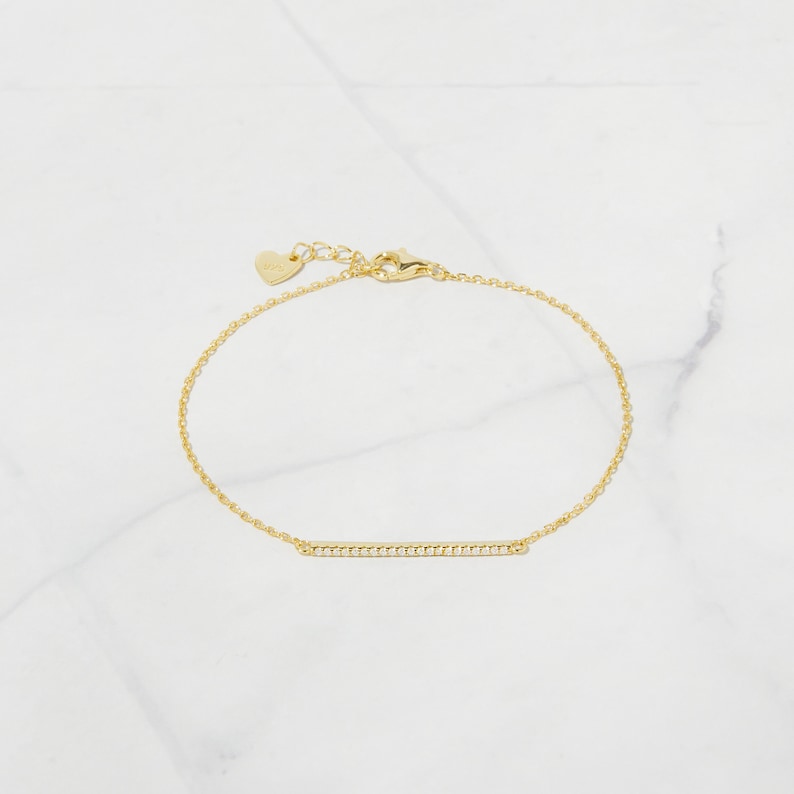 May include: A gold chain bracelet with a thin bar charm set with small clear stones.