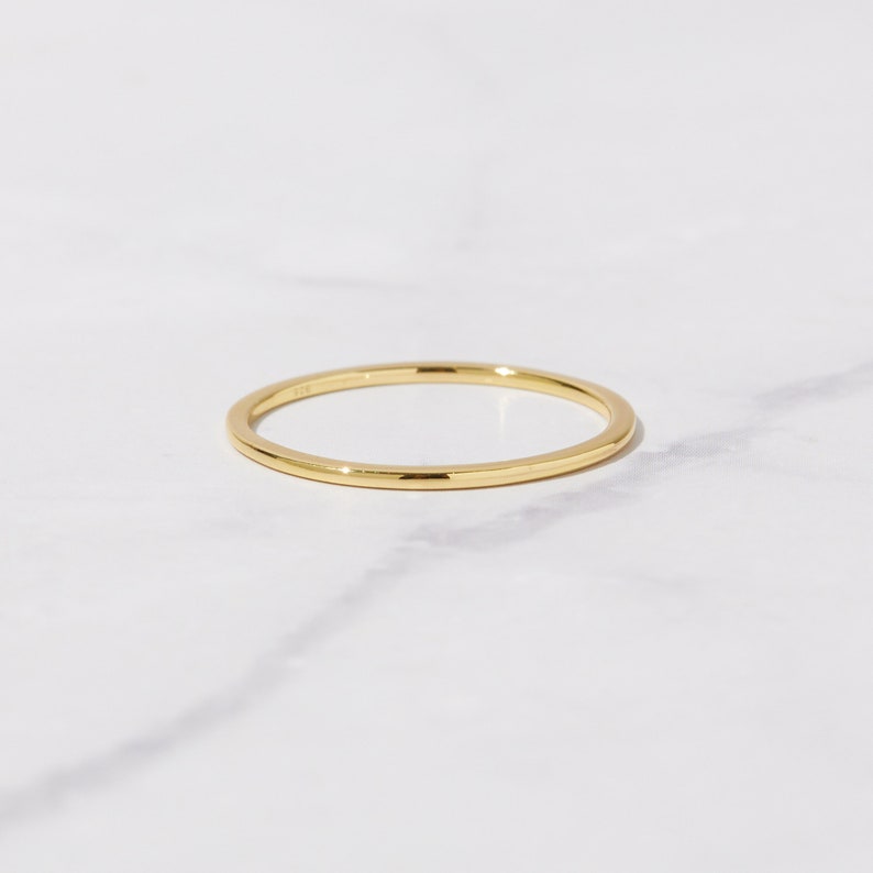 May include: A simple gold band ring. The ring is thin and has a smooth, polished finish.