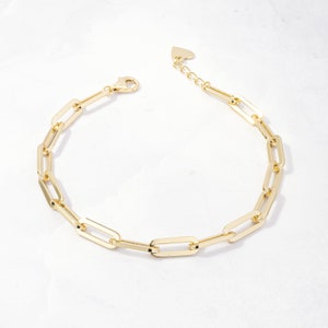 May include: A gold-toned chain bracelet with a heart-shaped clasp. The bracelet is made of interlocking rectangular links.
