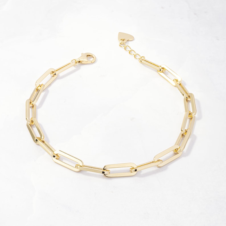 May include: A gold-toned chain bracelet with a heart-shaped clasp. The bracelet is made of interlocking rectangular links.