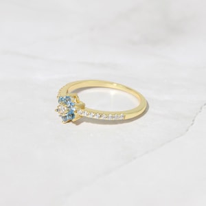 May include: A gold ring with a cluster of blue and white gemstones. The ring has a thin band with a row of small white gemstones.