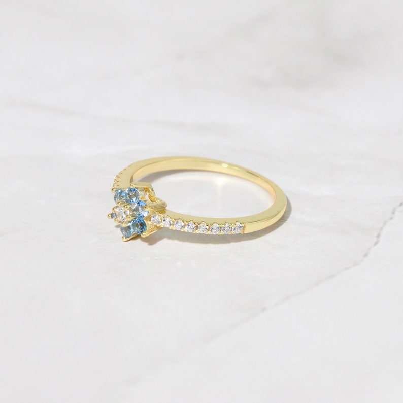 May include: A gold ring with a cluster of blue and white gemstones. The ring has a thin band with a row of small white gemstones.